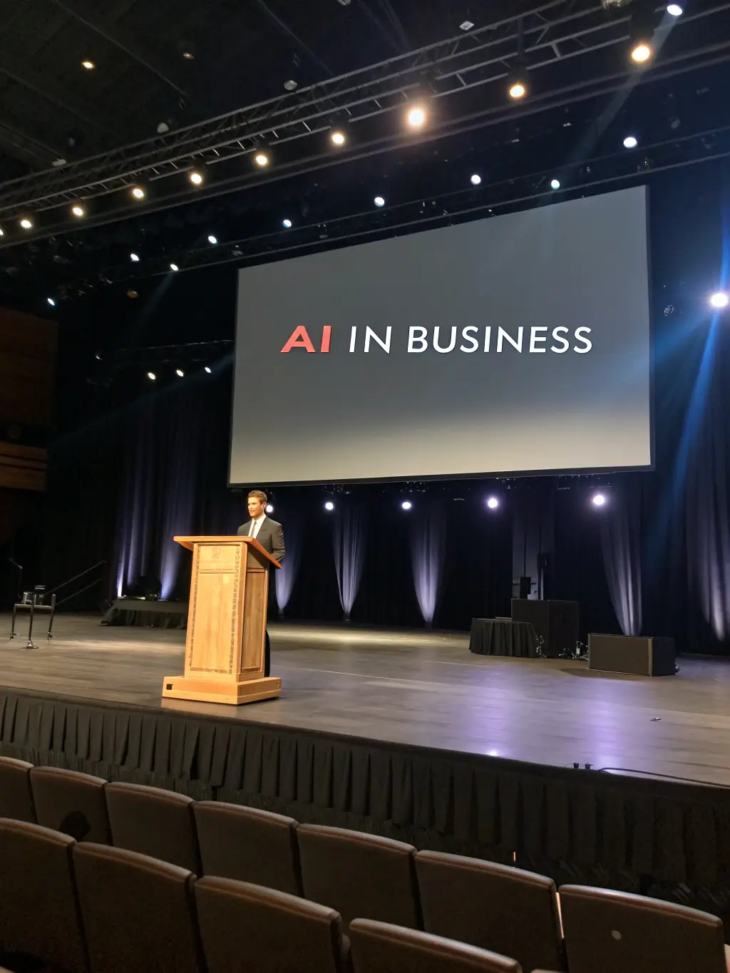 A modern conference hall filled with attendees listening to a keynote speaker at a UK tech summit, focusing on AI innovation.